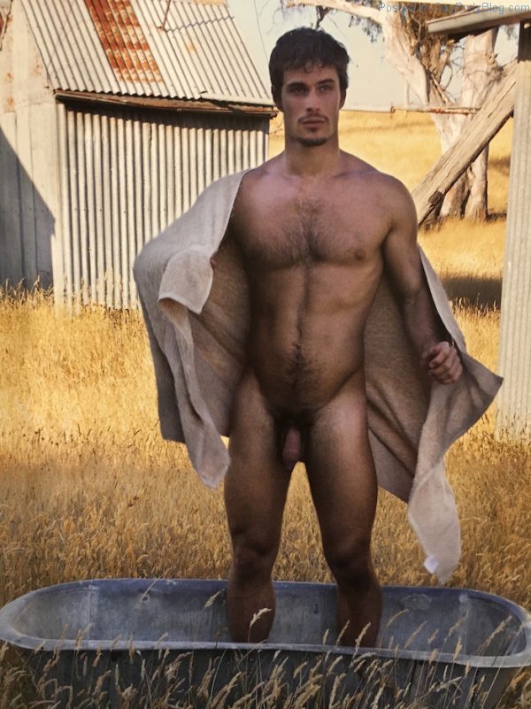 Brandy Martignago stands naked in a small metal tub on what looks like a farm, surrounded by golden grass.