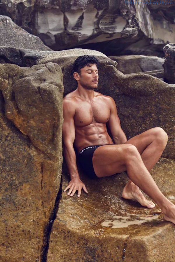 Male model Daniel Garofali at the beach meditating against the rocks