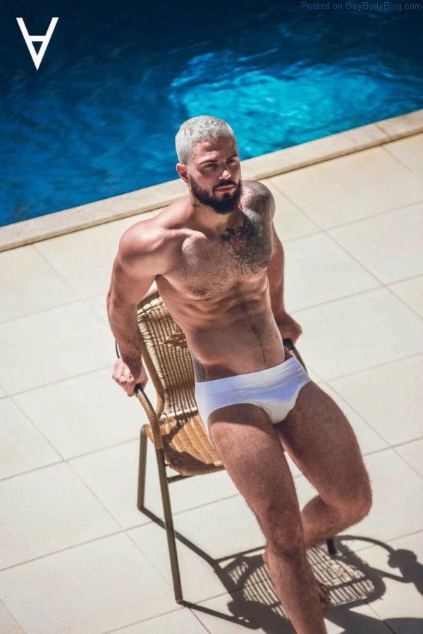 Male model Adriano Cardoso leaning on a chair beside a blue pool in the sun