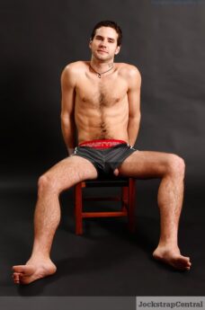 man sitting on a chair in shorts with his uncut penis peeking out of a leg hole