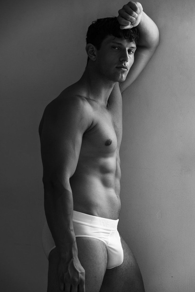 Black and white photo of Josh Ivory wearing just white underwear while leaning against a wall