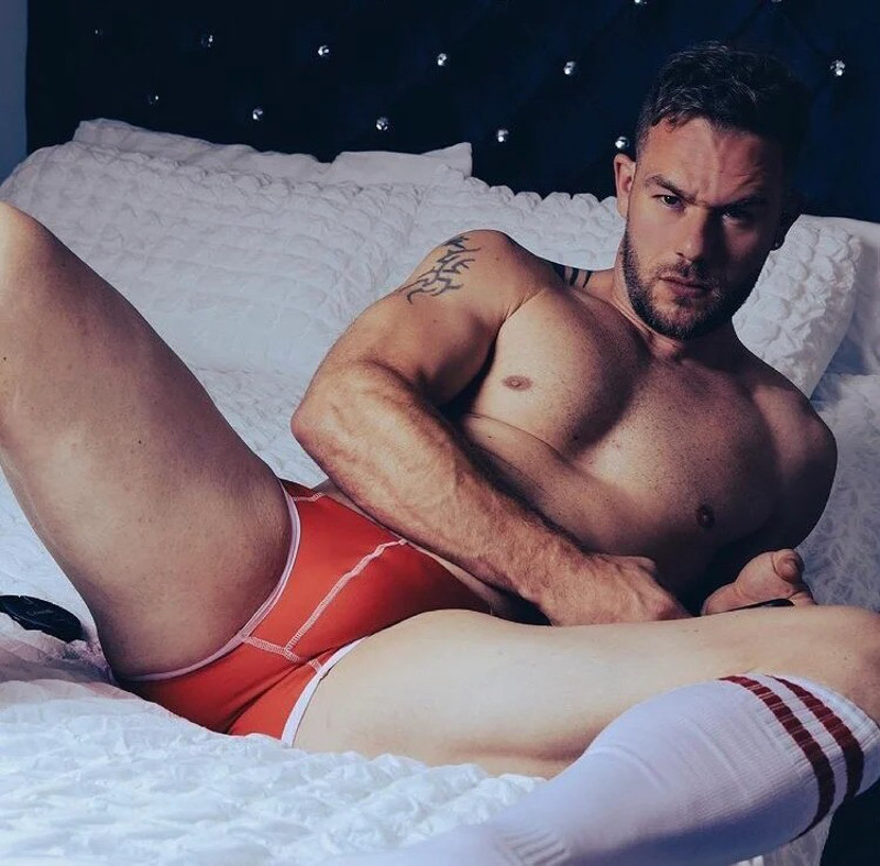 Dean Dancer in red bulging briefs laying on a bed.